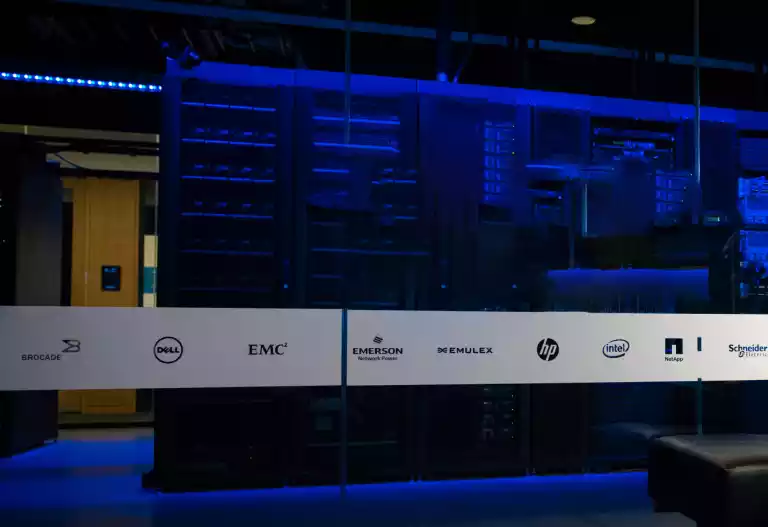 Modernes Rechenzentrum mit Serverracks unter blauem Licht und Logos bekannter Technologieunternehmen.