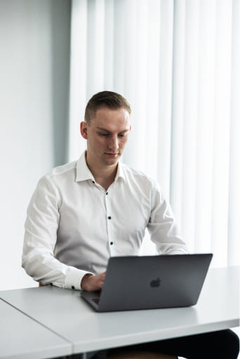 Tobias Lechner arbeitet an einem MacBook Pro, während er an einem Tisch sitzt und ein weißes Hemd trägt.