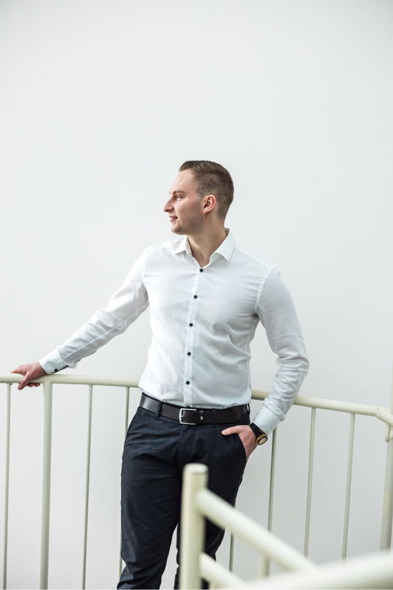 Tobias Lechner lehnt in weißem Hemd und einer dunklen Hosen an einem weißen Geländer einer Treppe im Büro von Lechner IT-Dienstleistungen.