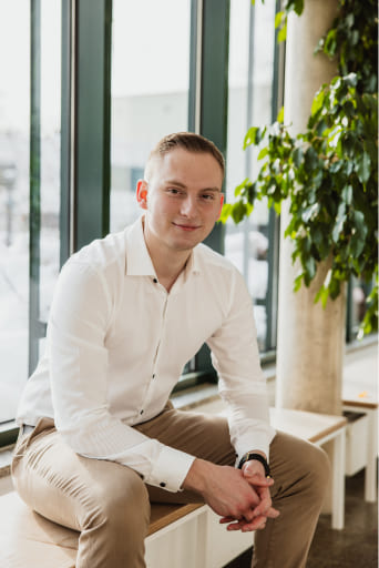 Herr Tobias Lechner, Inhaber von Lechner IT-Dienstleistungen, sitzt lächelnd in einem hellen Raum. Er trägt ein weißes Hemd und eine Hose.