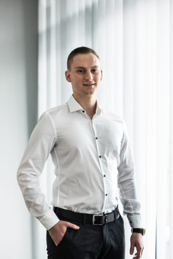 Tobias Lechner, Inhaber von Lechner IT-Dienstleistungen, posiert professionell vor einem Fenster mit vertikalen Jalousien.