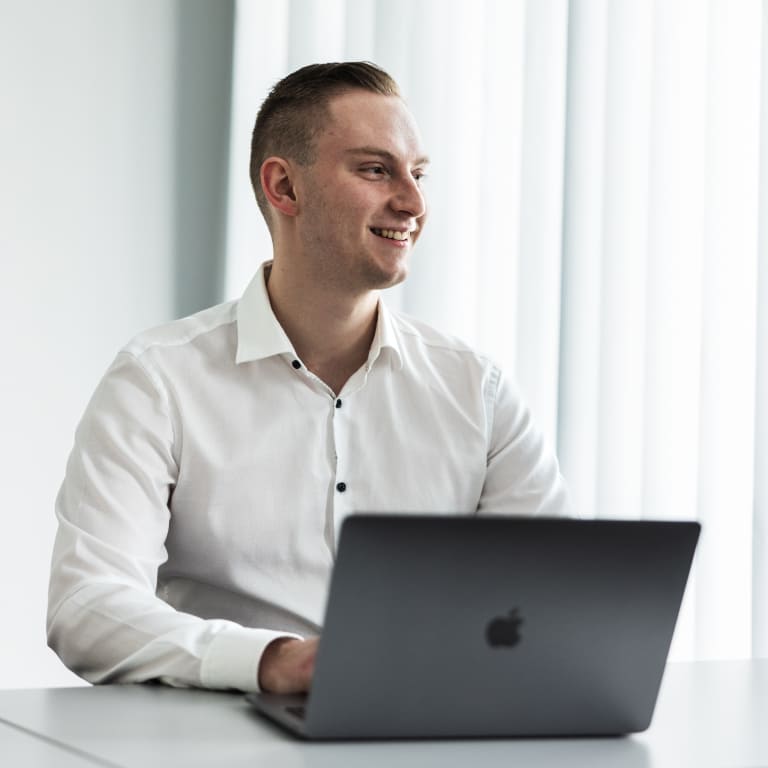 Tobias Lechner arbeitet an einem MacBook Pro an einem Tisch und lächelt seiner Kundin zu.